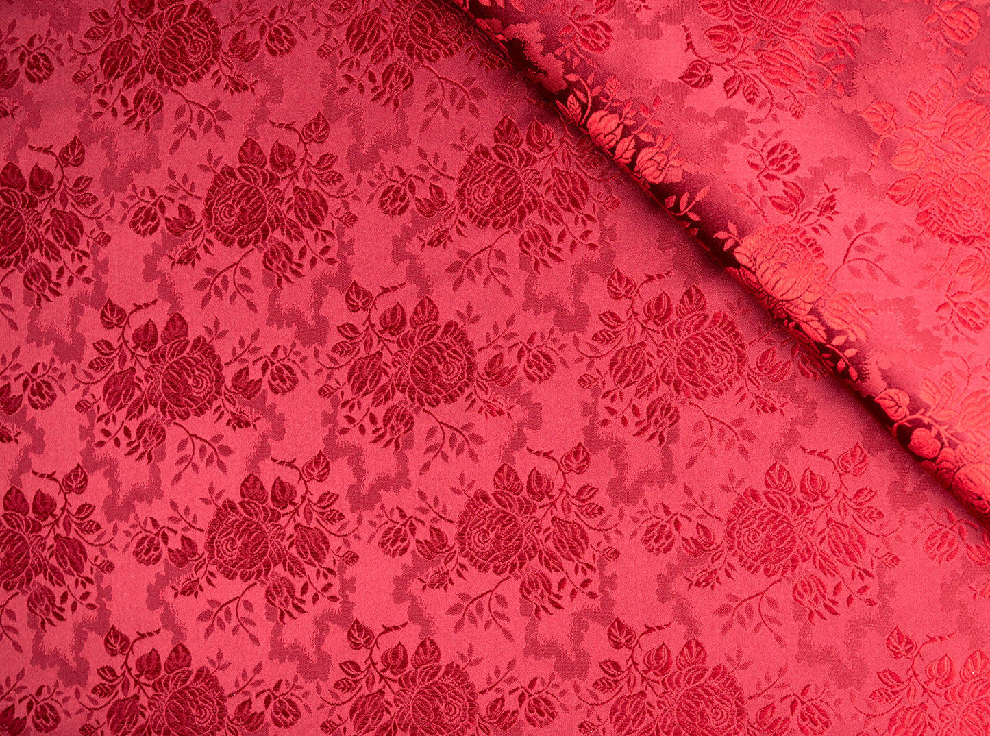 Rødt silke stoff med litt dypere rødfarge i bakgrunnen enn på rosene