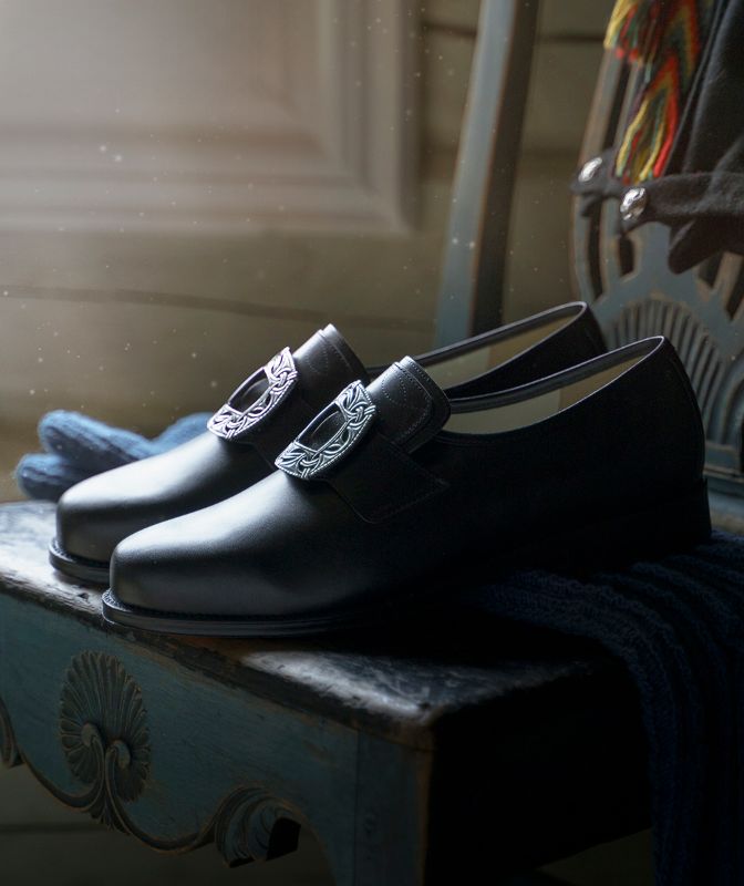 Ett par lars-sko på en utskjæret trestol med hosebånd i bakgrunnen.